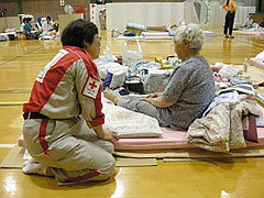 布団の上に座る被災者に問診する救護スタッフの様子